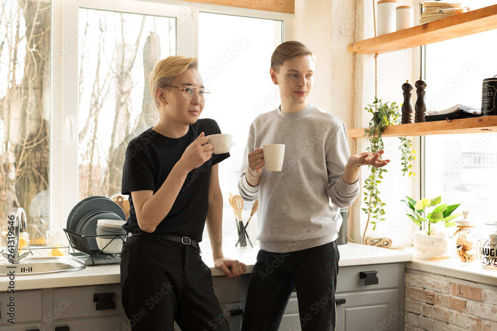 Fototapeta premium Portrait of international gay couple in casual clothes in the morning at home in the kitchen