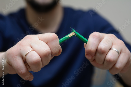In the foreground a young man's hands breaking a pencil. concept - irritation and anxiety