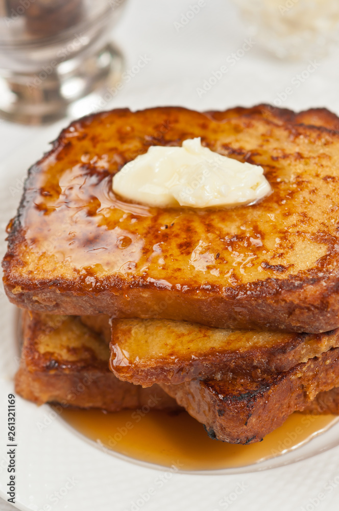 Top view, close distance of three slices fo freshly baked, homemade french toaast with pat of butter and covered with warm, maple syrup on a round white plate Top view, close distance of three slices fo freshly baked, homemade french toaast with pat of butter and covered with warm, maple syrup on a round white plate