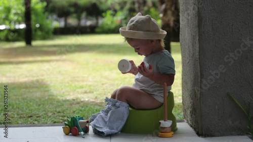 Sweet toddler boy, sitting on potty on a back porch in a holiday resort patio, playing with toys