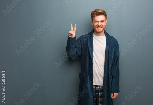 Young redhead man in pajama fun and happy doing a gesture of victory