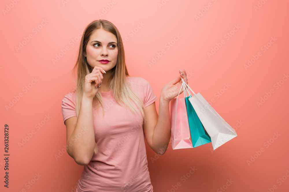 Young pretty russian girl doubting and confused. She is holding a shopping bags.