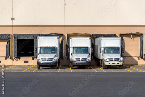 Small compact rigs semi trucks with box trailers standing in row at warehouse docks for loading cargo © vit