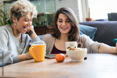 Two friends looking at a phone together at home