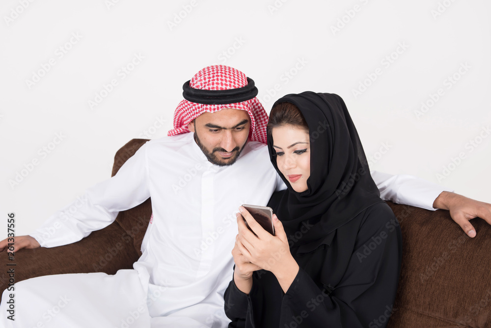 Arab muslim married couple using smart phone while sitting on sofa chair at home Arab muslim married couple using smart phone while sitting on sofa chair at home