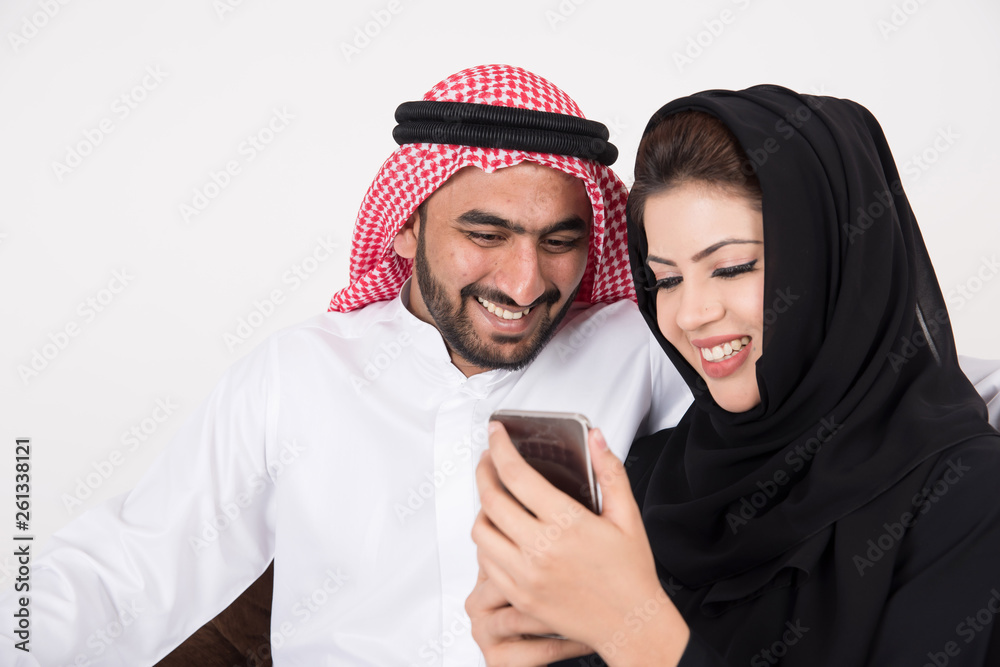 Arab muslim married couple using smart phone while sitting on sofa chair at home