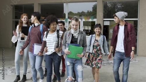 Medium shot of group of college students holding files and walking together in campus