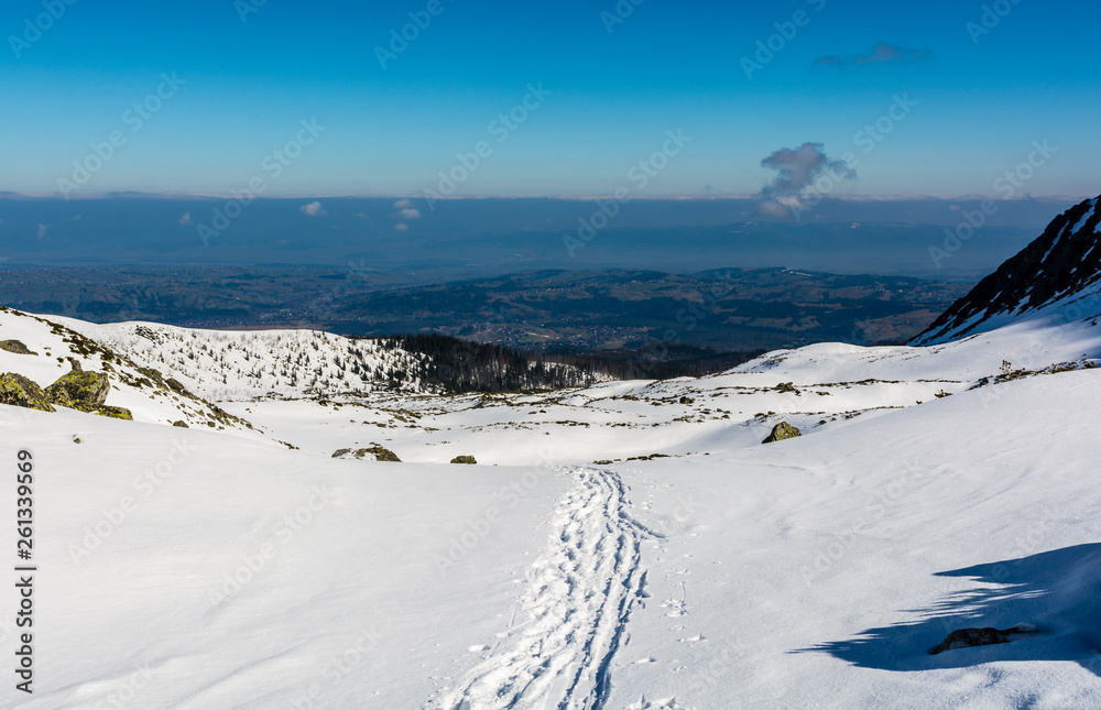 Traces of hikers and skiers on the snow forming a path through the valley with a view of the smog above the lowlands.