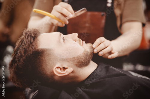Man Barber shaves beard of client on chair Barbershop