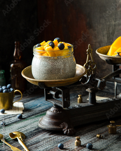 Homemade glass bowl with super food chia pudding with cut mango, blueberries on top stand on vintage scales