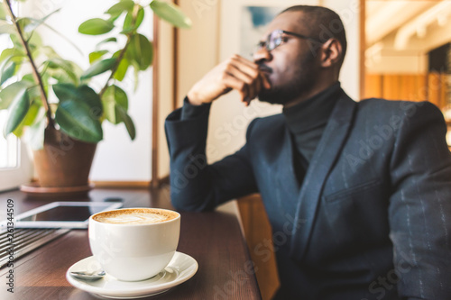 Young handsome dark-skinned businessman drinks coffee in a cafe.
