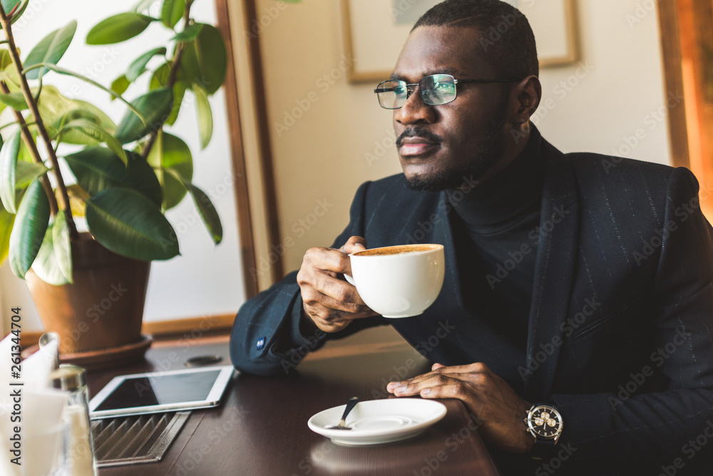 Young handsome dark-skinned businessman drinks coffee in a cafe. Young handsome dark-skinned businessman drinks coffee in a cafe.