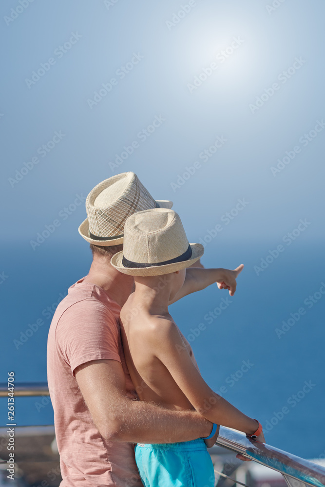Son and dad relaxing on hotel balcony on summer holidays. They are pointing to something ahead.