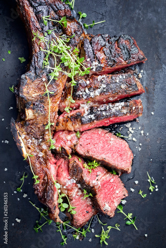 Traditional barbecue dry aged wagyu tomahawk steak sliced salt and herb as top view on a rustic old black board