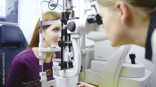 Fototapeta Naklejka Na Ścianę i Meble -  Female optometrist looking inside the device of patient eyeballs