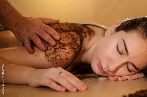 lateral view of a beautiful woman in spa salon having spa therapy with coffee done by a masseur