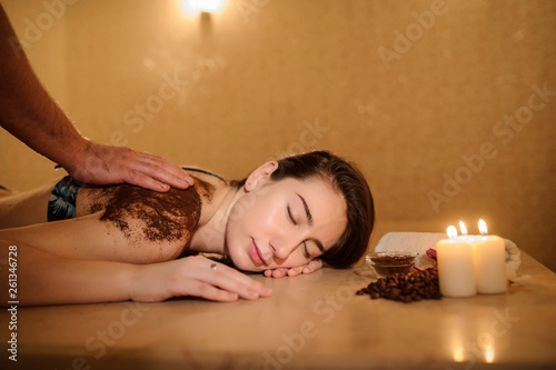 lateral view of a beautiful woman in spa salon having spa therapy with coffee done by a masseur