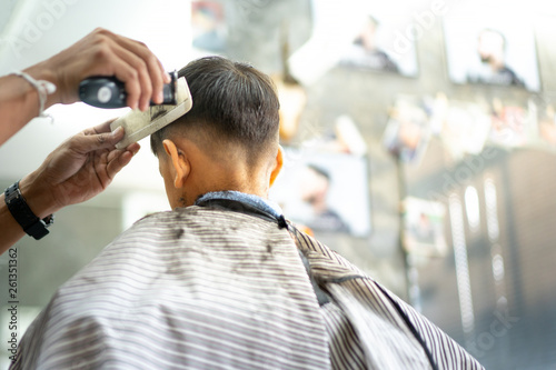 A little boy client getting haircut by professional hairdresser with shaving and white comb at the barbershop barber salon.