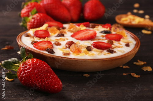 Bowl of yogurt with strawberries and granola muesli, over a white wood background.