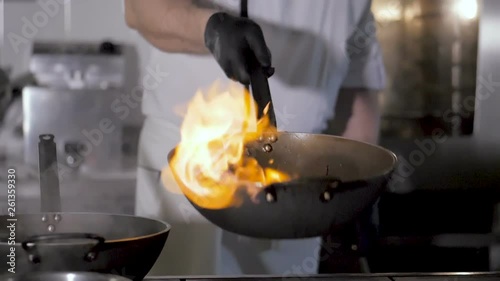 Chefs cooks and doing flambe on vegetables in wok on restaurant kitchen