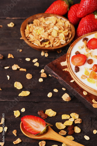 Bowl of yogurt with strawberries and granola muesli, over a white wood background.