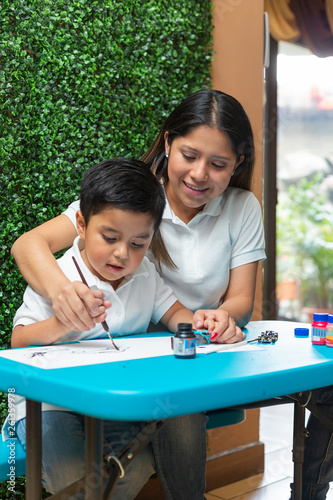 mom helps her 4-year-old son paint with a brush photo