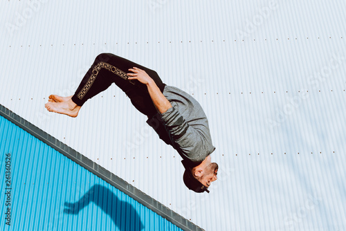 Side view of barefoot guy in stylish outfit performing flip near wall of modern building on city street