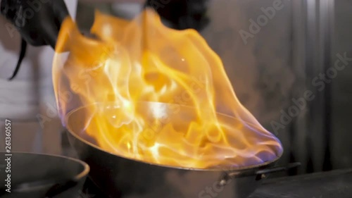 Chefs cooks and doing flambe on vegetables in wok on restaurant kitchen