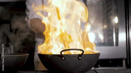 Chefs cooks and doing flambe on vegetables in wok on restaurant kitchen