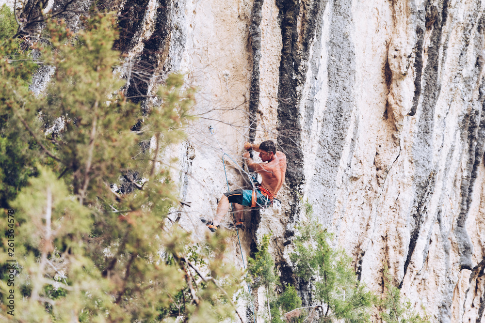 Side view of unrecognizable male in shorts climbing up rough cliff on sunny day in countryside Side view of unrecognizable male in shorts climbing up rough cliff on sunny day in countryside