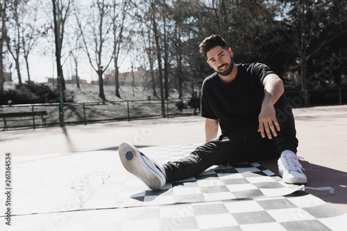 Young bearded guy in eyeglasses and casual wear sitting in park in sunny weather