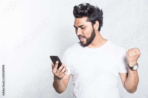 Happy young man holding smartphone and celebrating his success. © xartproduction