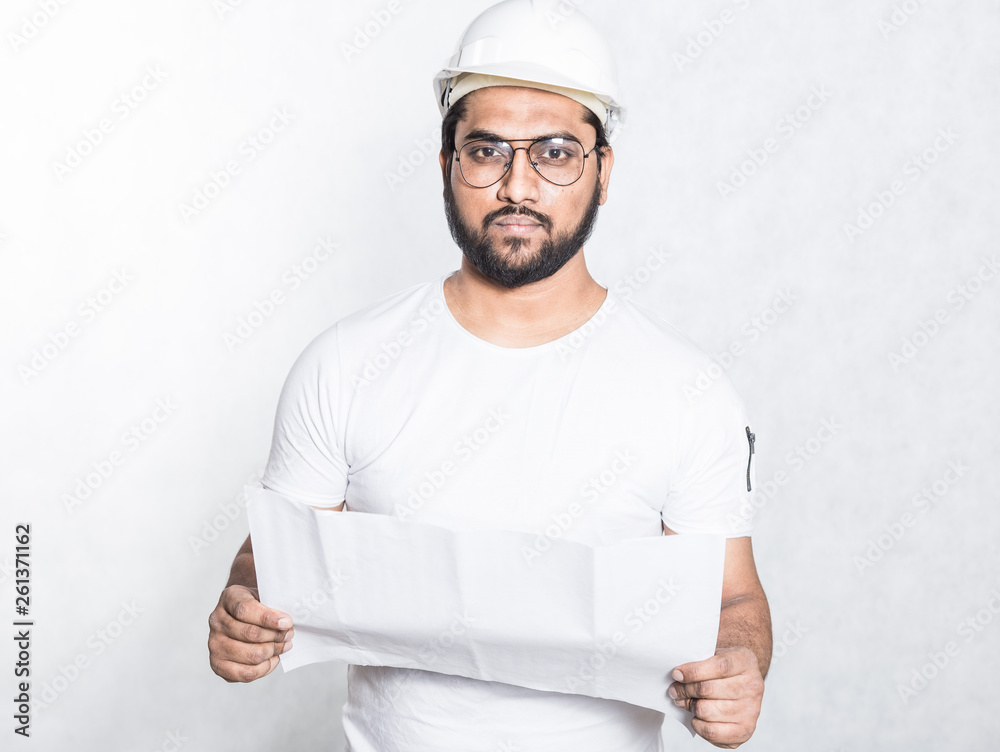 A young construction worker with glasses and a white protective helmet examines a drawing of a building. A young construction worker with glasses and a white protective helmet examines a drawing of a building.