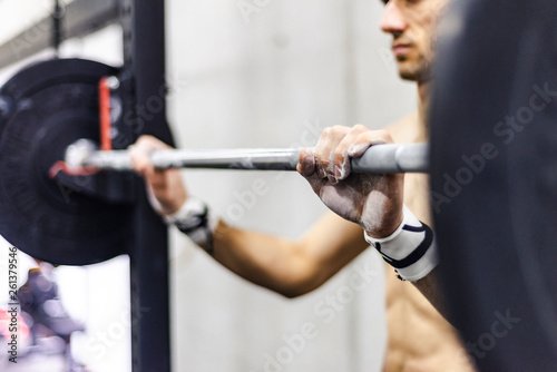 Crop shirtless male lifting barbel wit h weights in gym on blurred background photo