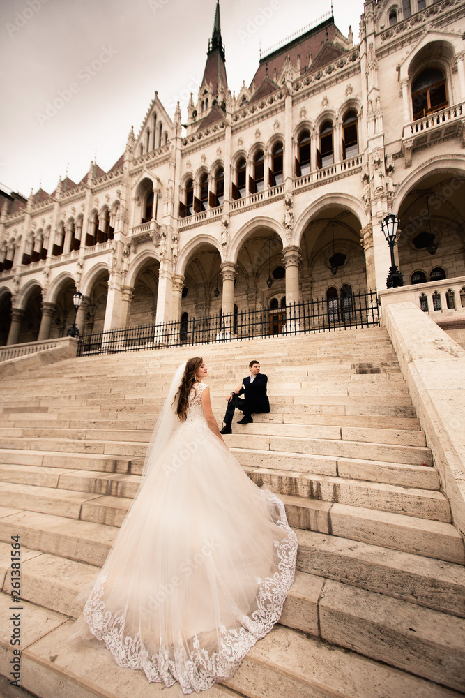Obraz premium Bride and groom hugging in the old town street. Wedding couple walks in Budapest near Parliament House. Bride and groom on the stairs