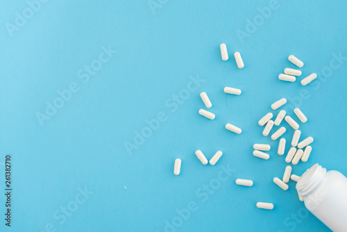Pills spilled out of white bottle on blue background. Medical, pharmacy and health care concept. Copy space.