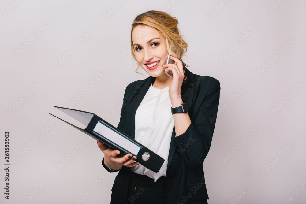 Portrait joyful blonde businesswoman talking on phone, holding folder, smiling to camera isolated on white background. Wearing white shirt and black jacket, modern office worker, elegant, career Portrait joyful blonde businesswoman talking on phone, holding folder, smiling to camera isolated on white background. Wearing white shirt and black jacket, modern office worker, elegant, career