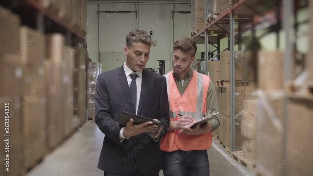 Medium shot of warehouse worker and businessman discussing with digital tablet and clipboard while maintaining records in warehouse Medium shot of warehouse worker and businessman discussing with digital tablet and clipboard while maintaining records in warehouse