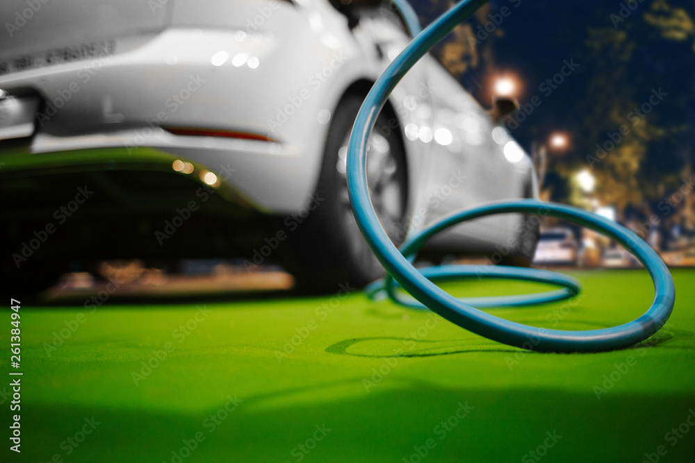Naklejka premium Electric vehicle at charging station. Focus on cable