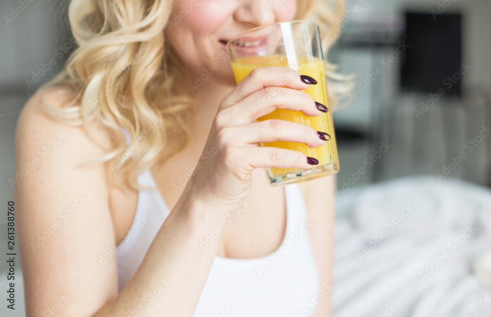Attractive blonde woman sits on the edge of the bed at home and holds a stocker with orange juice in her hand. Morning mood and vigor Attractive blonde woman sits on the edge of the bed at home and holds a stocker with orange juice in her hand. Morning mood and vigor