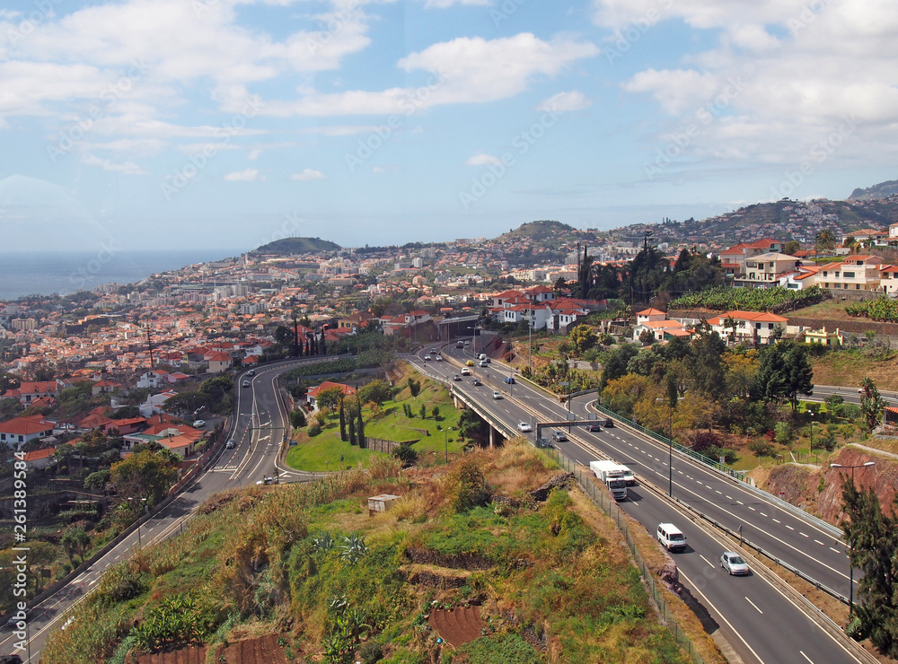 an aerial cityscape view of funchal showing traffic on the main VR1 motorway running into the city with the coast visible in the distance