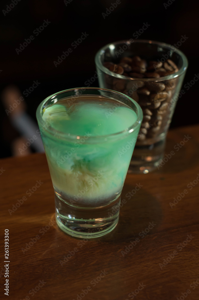 high angle view of shot glass with blue alcohol drink near glass with coffee beans on wooden table in bar high angle view of shot glass with blue alcohol drink near glass with coffee beans on wooden table in bar
