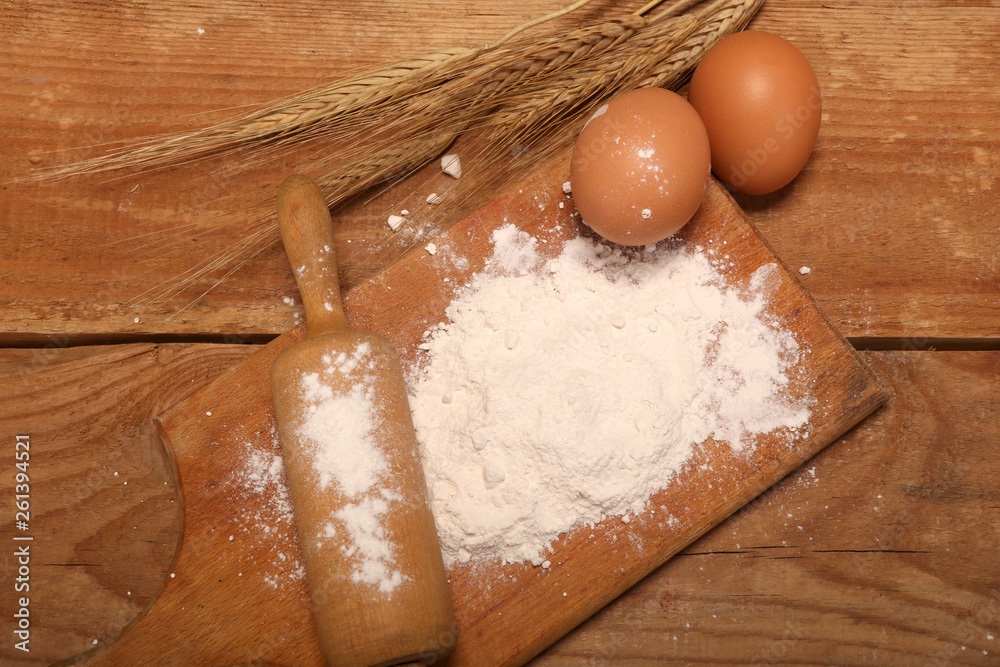Kitchen rolling pin, wooden board with flour on wooden background, ears and eggs for making bread on table. Kitchen rolling pin, wooden board with flour on wooden background, ears and eggs for making bread on table.