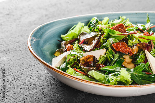 Healthy salad with grilled eggplant, greens, arugula, spinach, lettuce, dried tomatoes and cheese in plate over dark table. Healthy vegan food, clean eating, dieting.