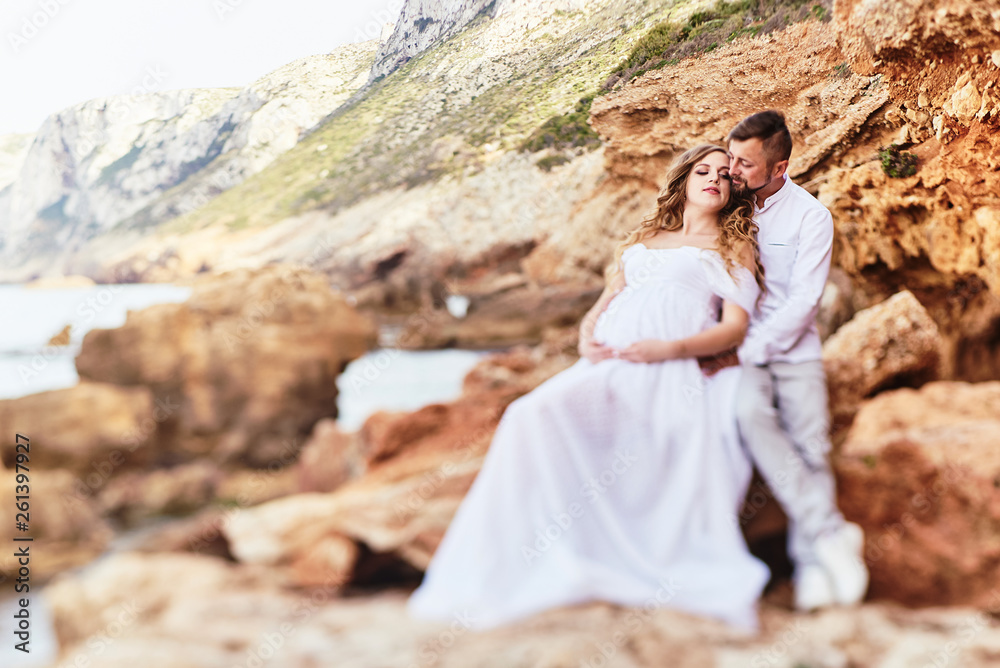 Fototapeta premium Young pregnant woman posing with her husband on the beach