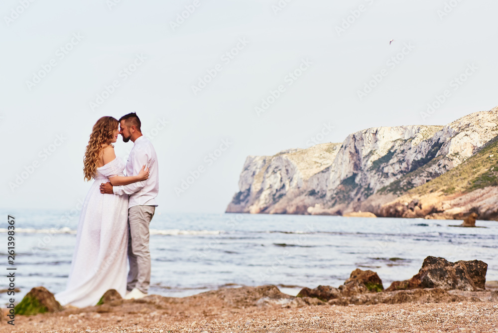 Young pregnant woman posing with her husband on the beach