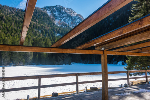 Snow covered lake with mountains in the background seen through the wooden roof structure