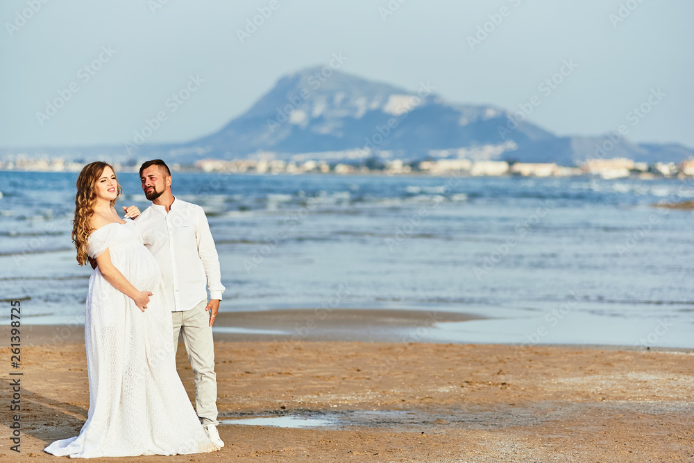 Young pregnant woman posing with her husband on the beach Young pregnant woman posing with her husband on the beach