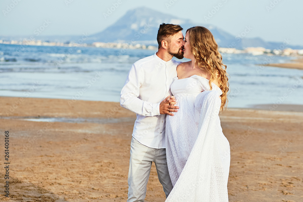 Young man kissing his beautiful pregnant wife in white dress