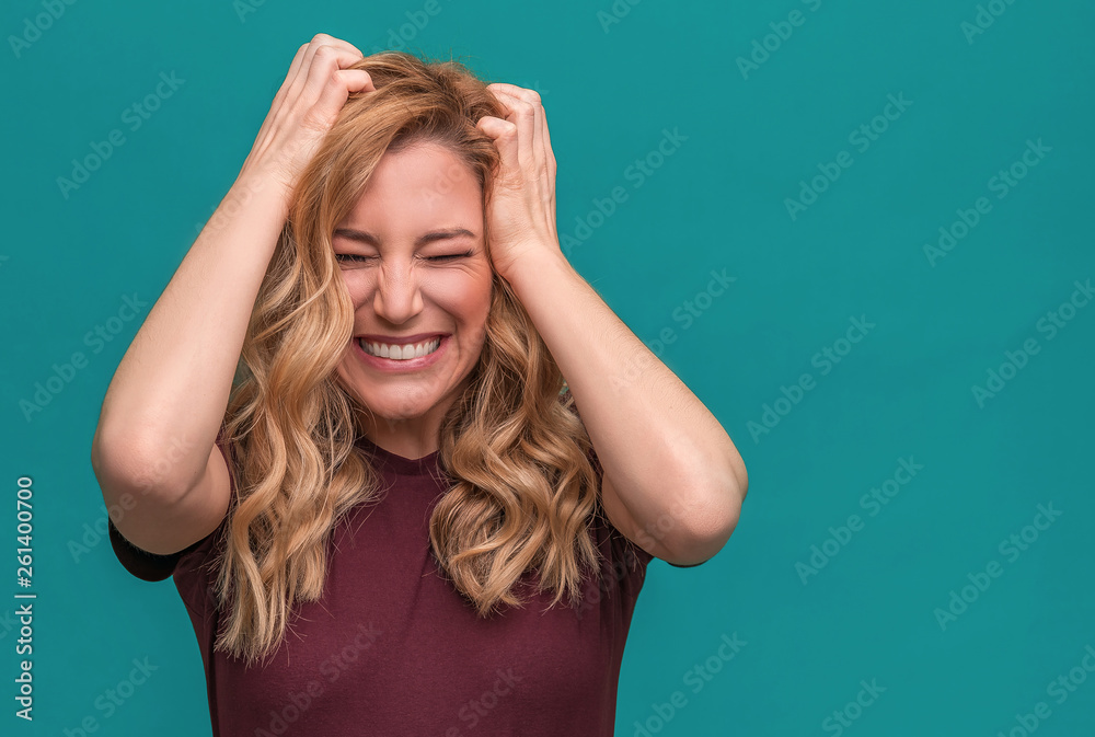 Attractive angry blonde girl angrily holds her head. Angry young woman on blue background.